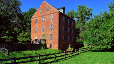 A red brick building with a steep roof, surrounded by lush greenery and a wooden fence.