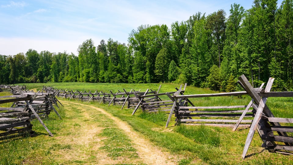 A rural landscape with a dirt path and wooden fences.