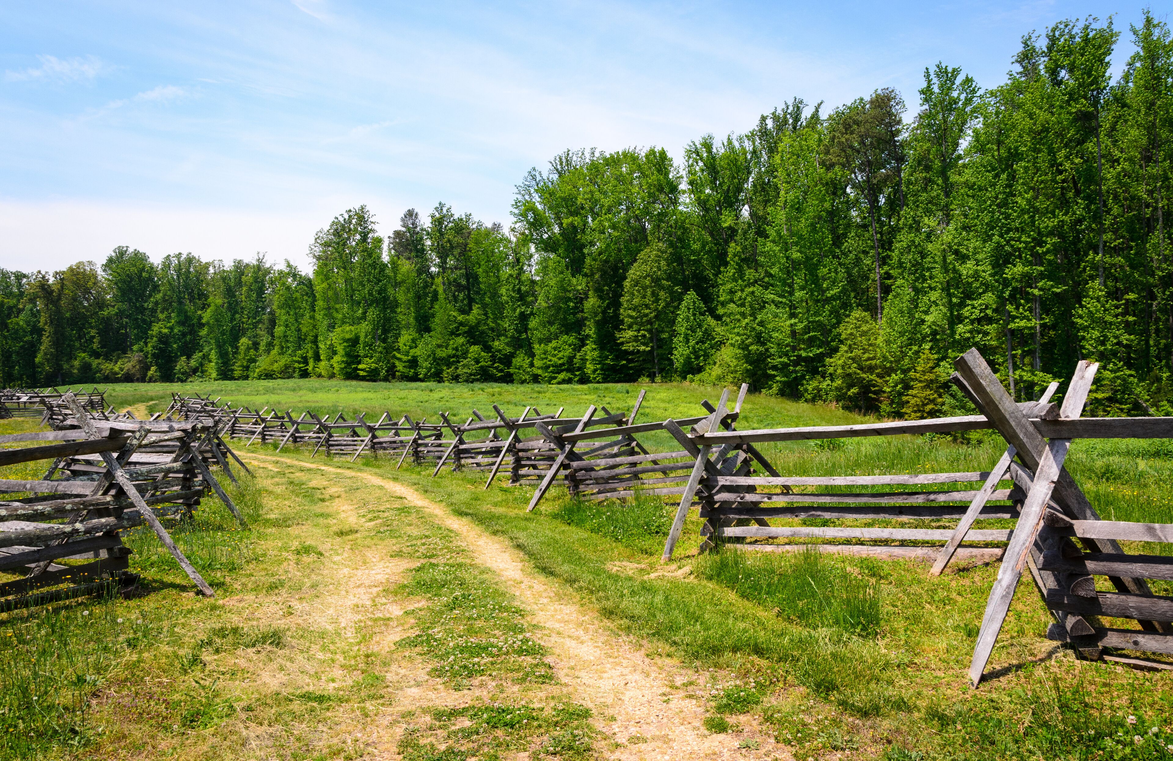 A rural landscape with a dirt path and wooden fences.