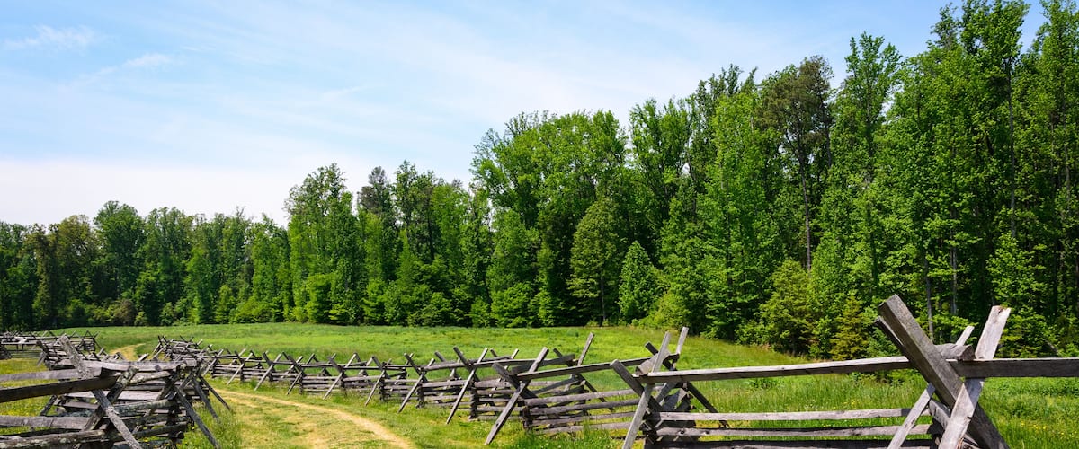 A rural landscape with a dirt path and wooden fences.