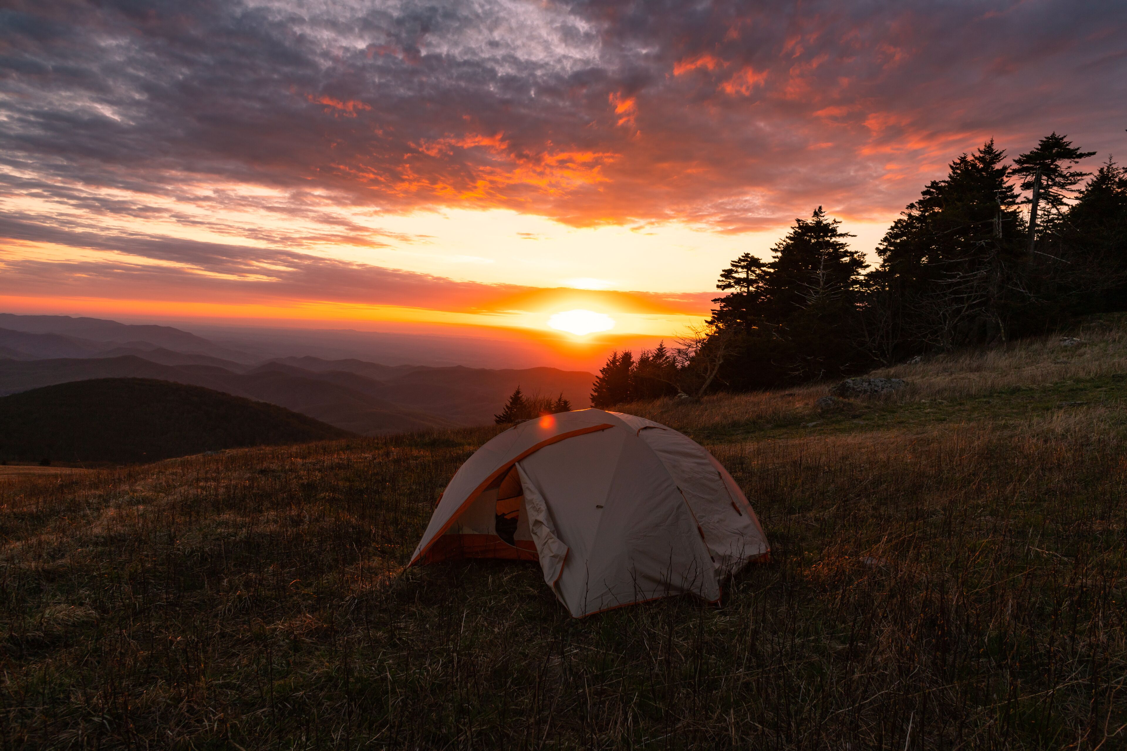 A tent on a grassy hill with a sunset in the background.