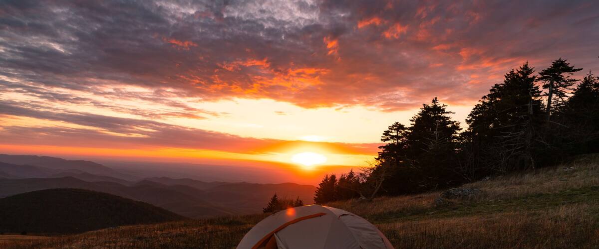 A tent on a grassy hill with a sunset in the background.