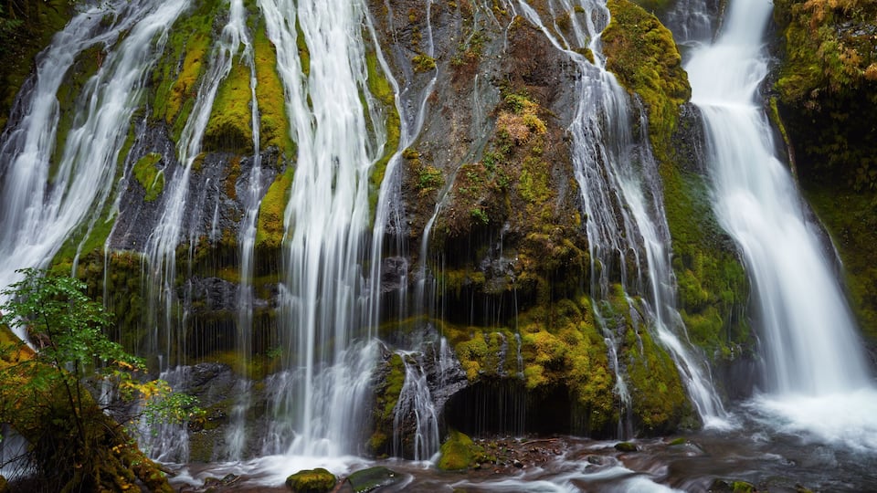 A multi-tiered waterfall with moss-covered rocks and a flowing stream at the base.