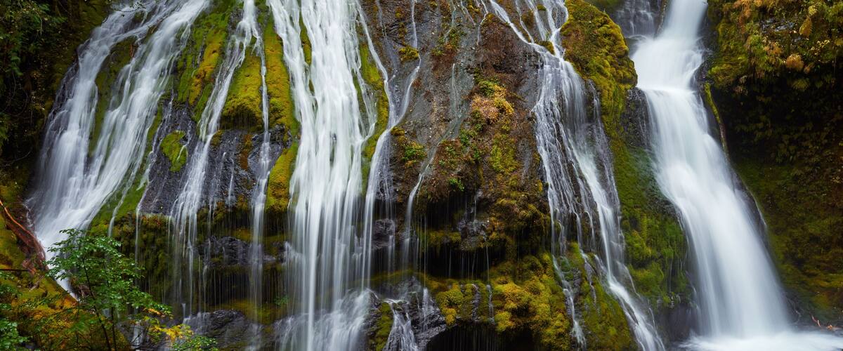 A multi-tiered waterfall with moss-covered rocks and a flowing stream at the base.