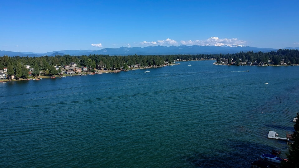 A large body of water with a forested shoreline, a small town, and snow-capped mountains in the distance.