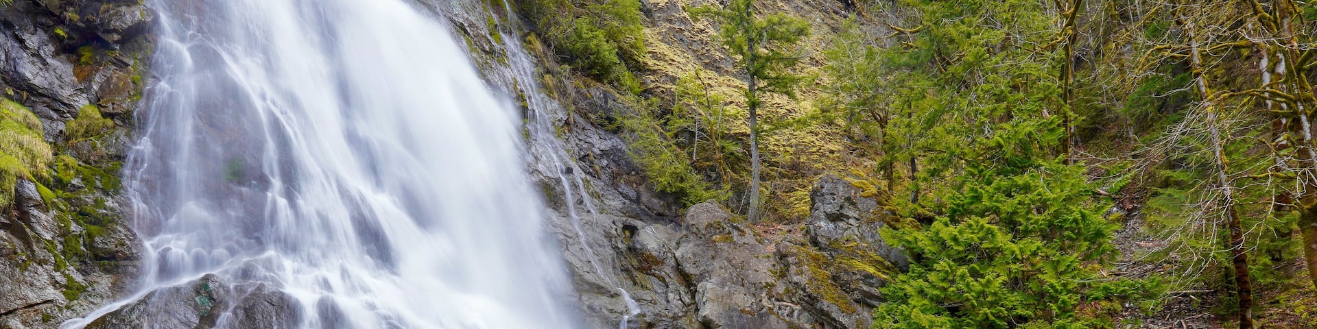 A waterfall cascading over rocks into a clear pool surrounded by forest.