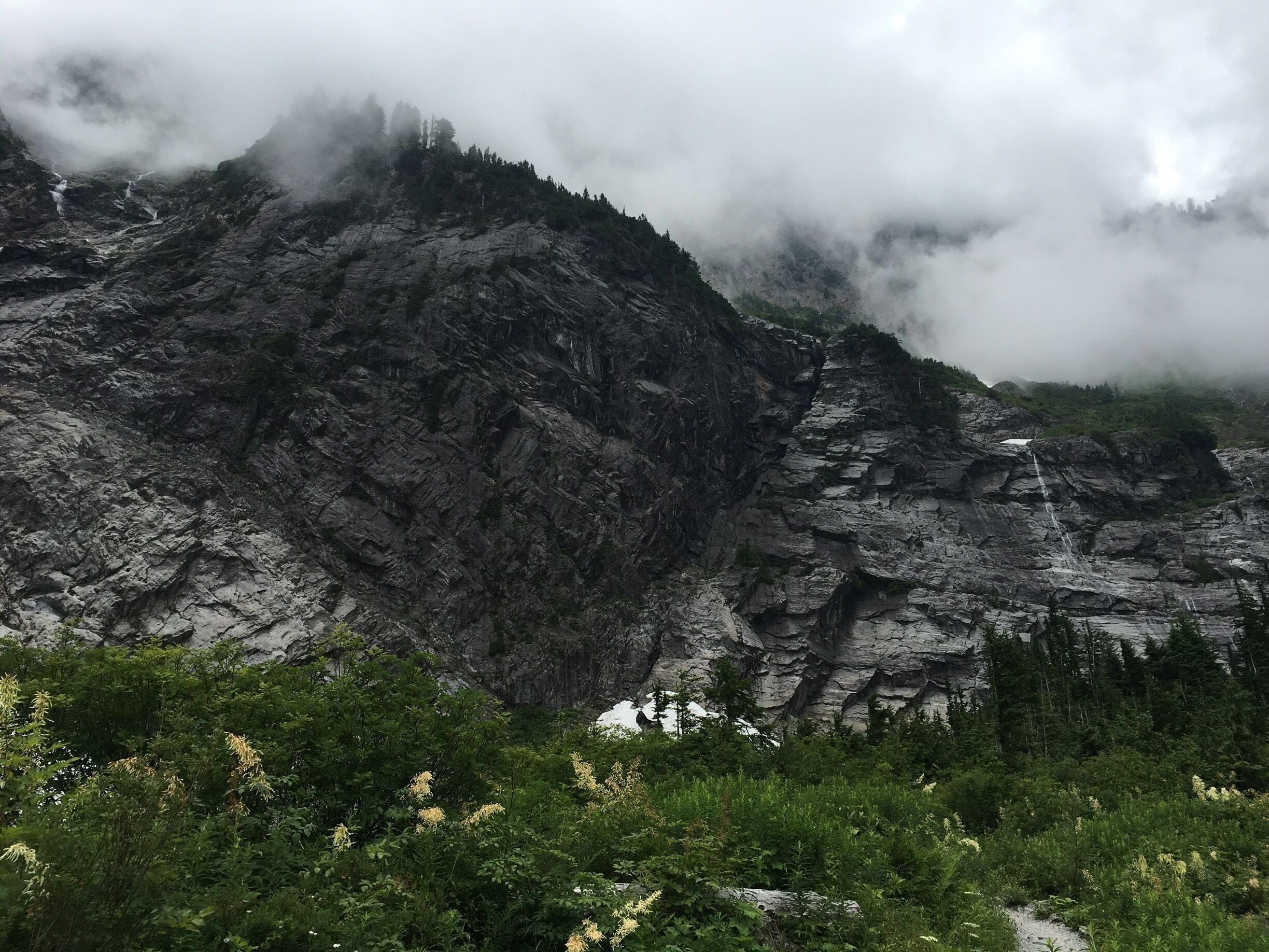 A rugged mountain landscape with dense vegetation at the base and a waterfall cascading down the rocky slope.