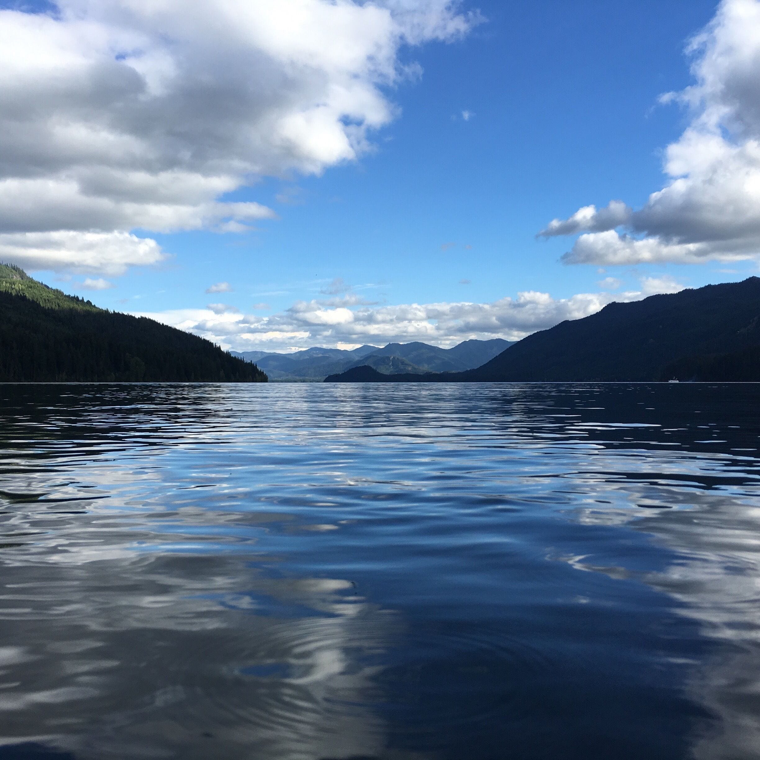A calm lake with mountains in the background and a partly cloudy sky.