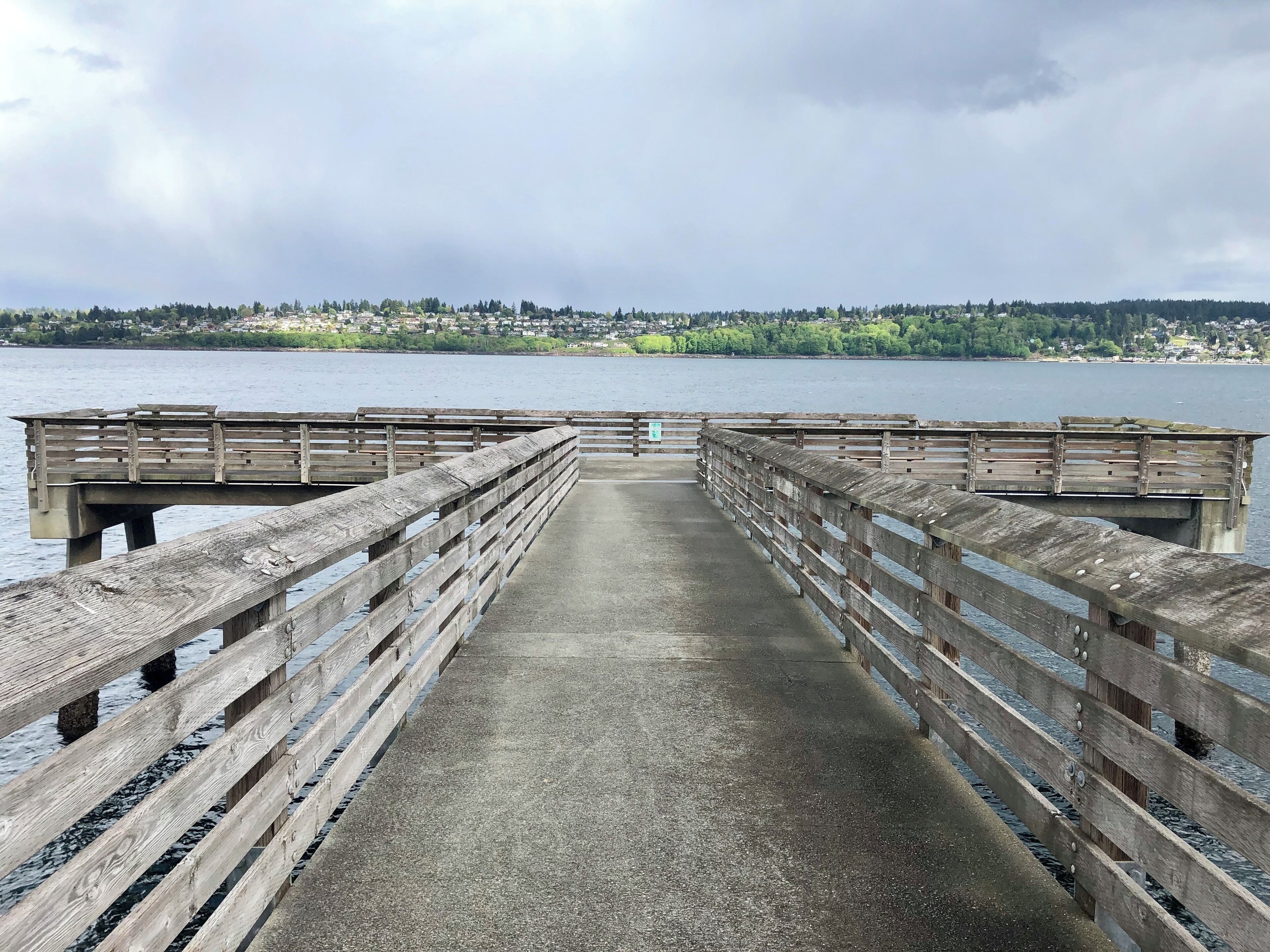 A wooden pier extending into a calm body of water with a distant shoreline.