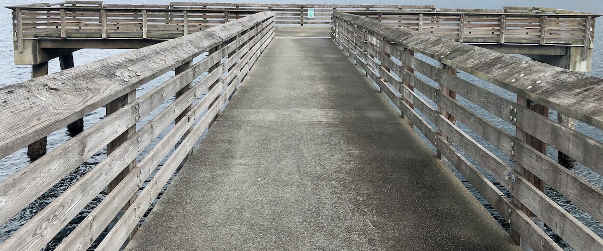A wooden pier extending into a calm body of water with a distant shoreline.