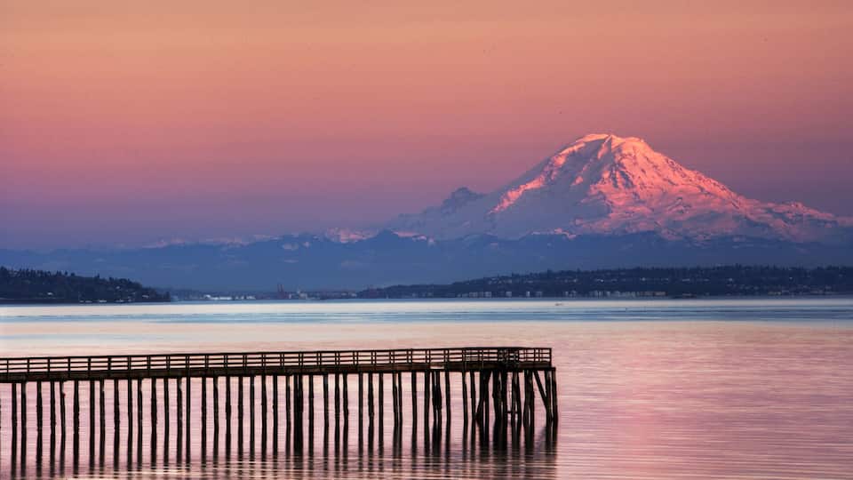 A mountain at sunset with a pier extending into calm water.