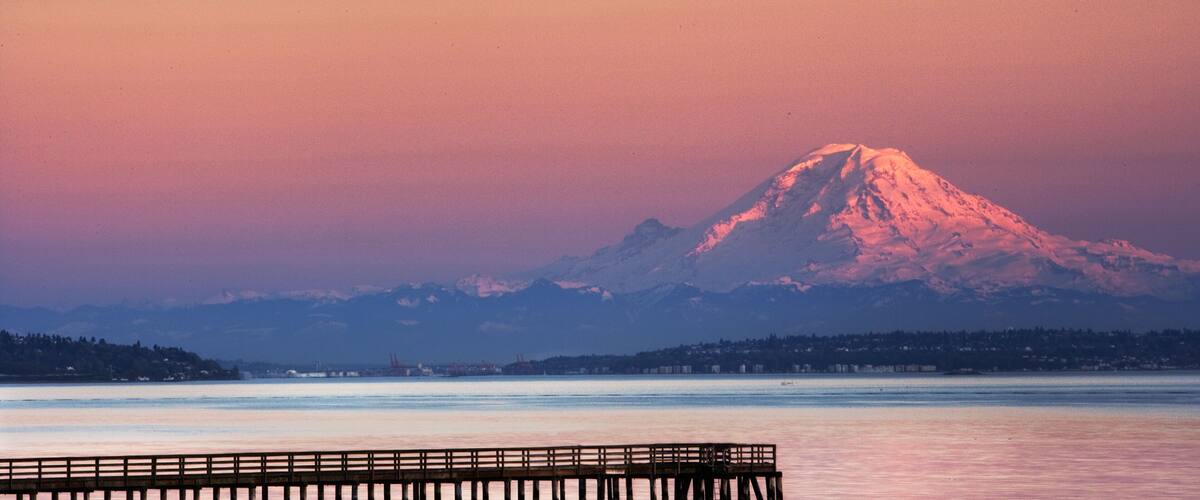 A mountain at sunset with a pier extending into calm water.