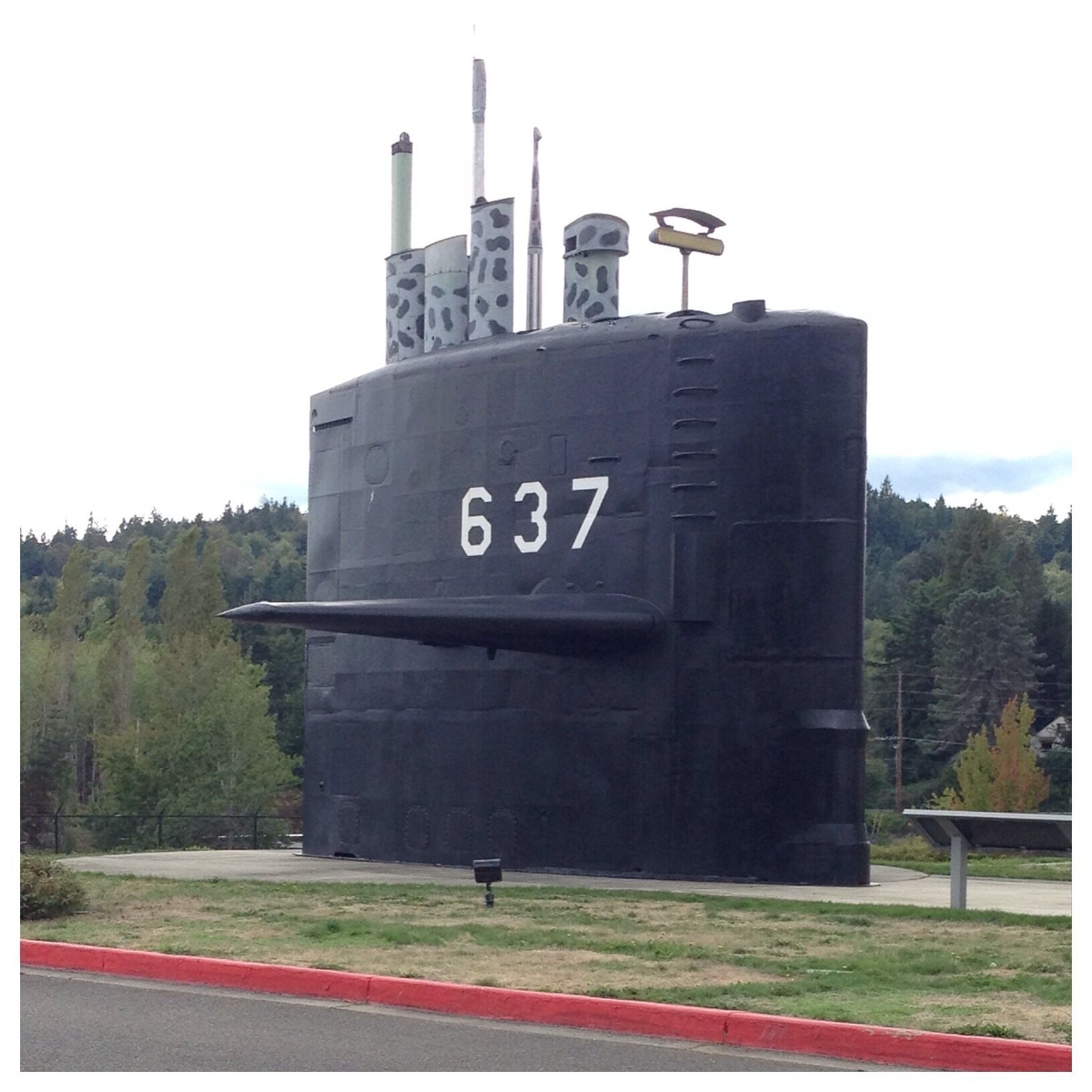 A large black submarine with the number 637 on its side, surrounded by a grassy area and trees.