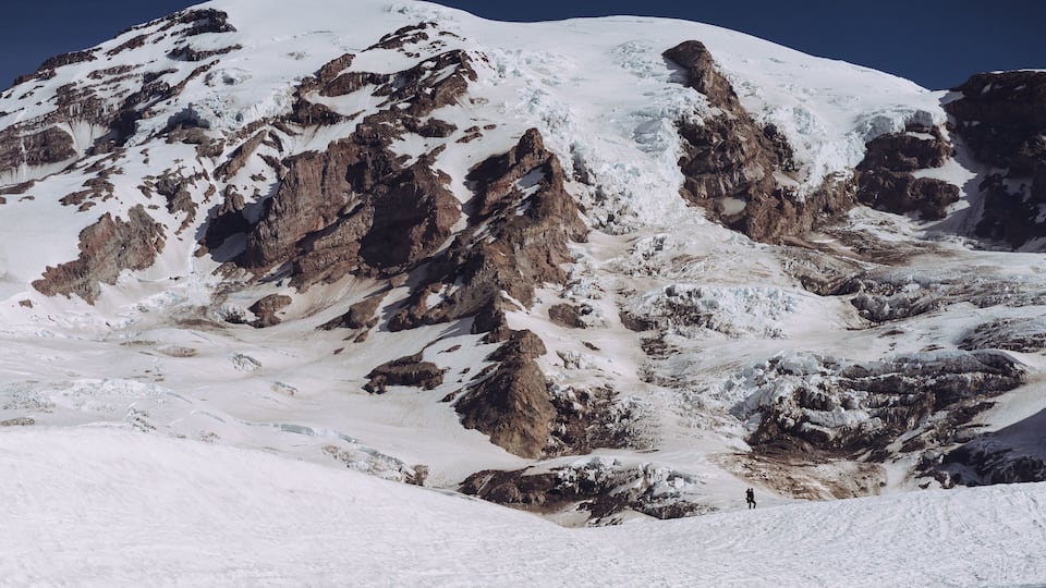 A snow-covered mountain with rocky outcrops and a clear sky.