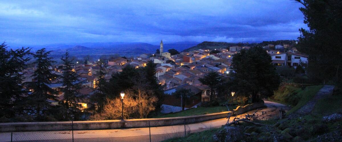 A town at dusk with a prominent church tower, surrounded by residential buildings and greenery.