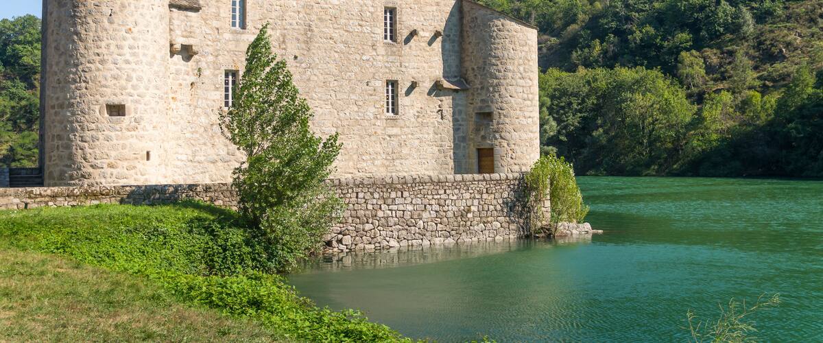 A stone castle by a river surrounded by greenery.