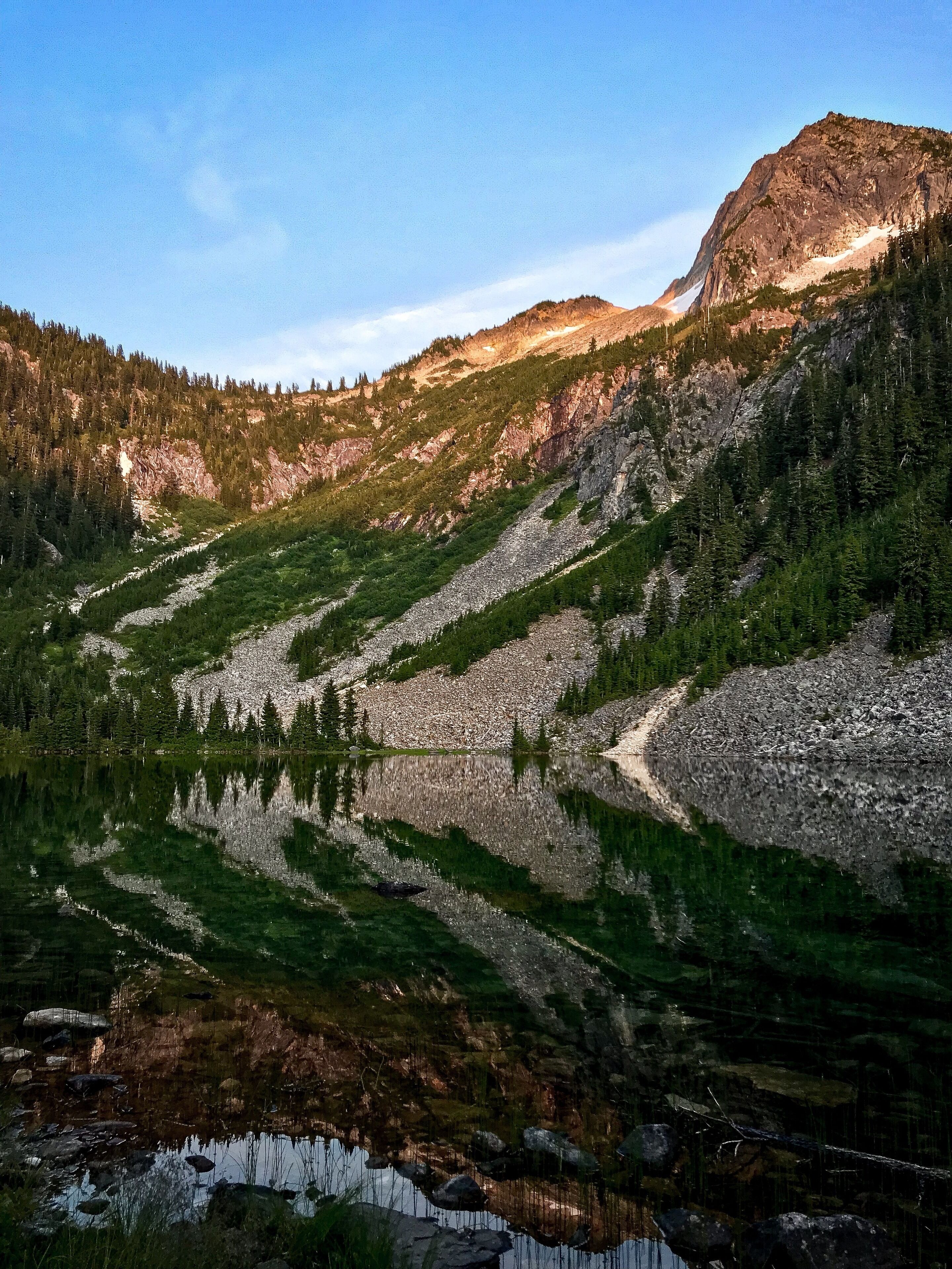 A mountain landscape with a clear lake reflecting the surrounding trees and rocky terrain.