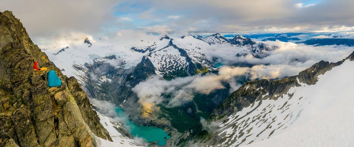 A mountain landscape with a rocky peak, a turquoise lake, and snow-covered peaks.