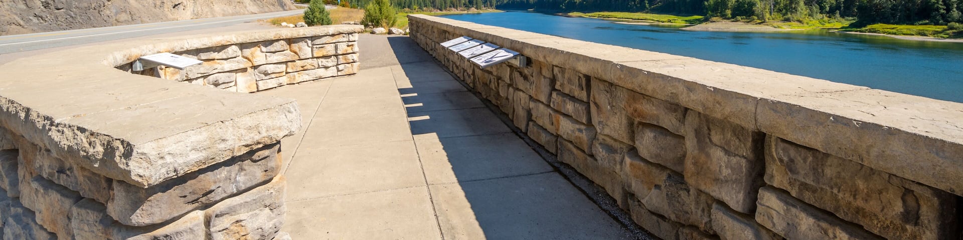 A stone bridge over a river with a forested hillside and mountains in the background.