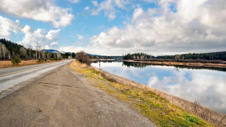 A road leading to a calm lake with mountains in the background.