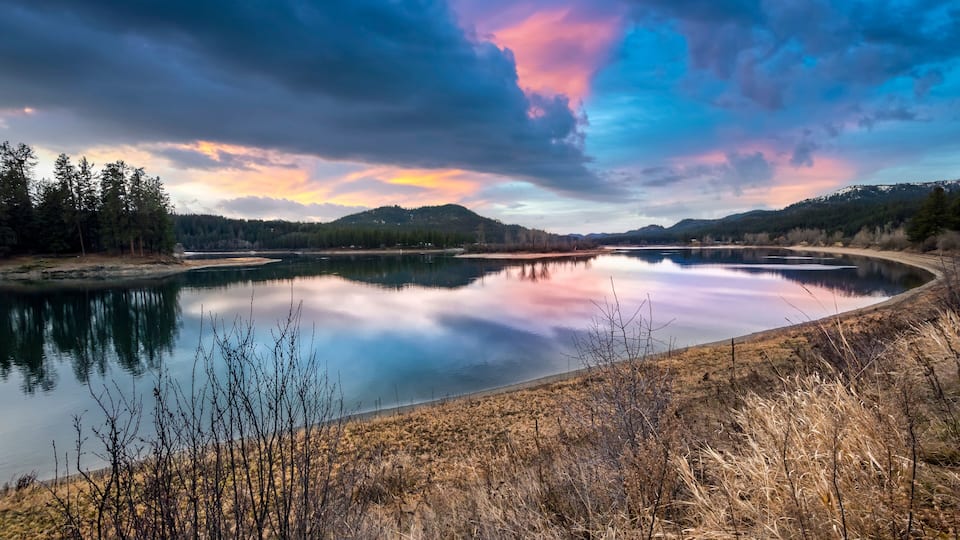 A calm lake reflecting the sky, surrounded by hills and sparse vegetation.