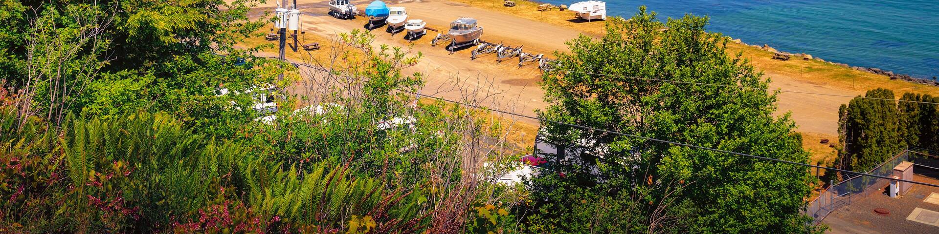 A coastal area with a marina, boats, RVs, and a forested hillside.