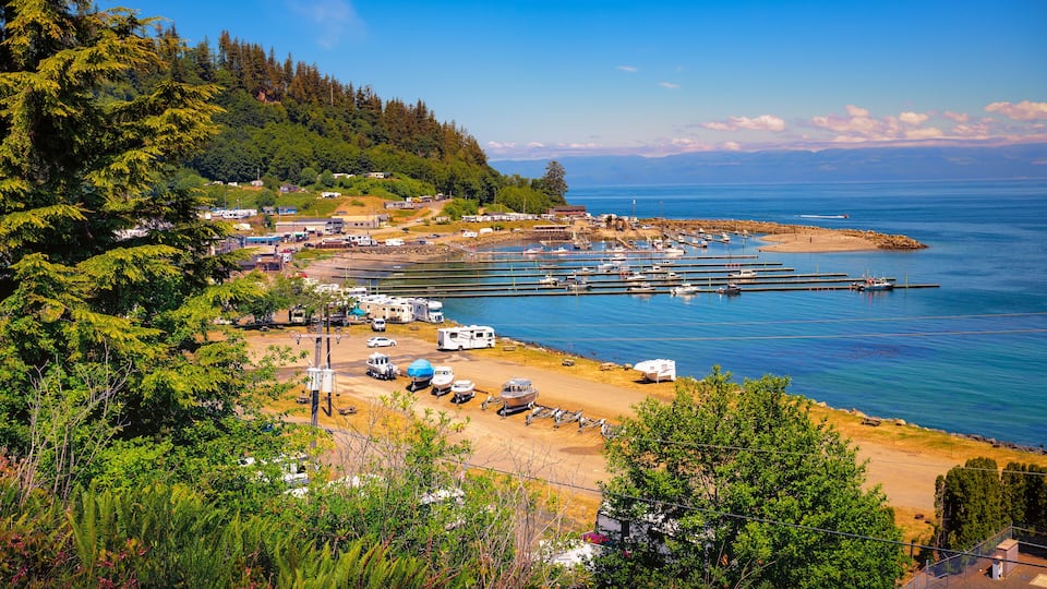 A coastal area with a marina, boats, RVs, and a forested hillside.