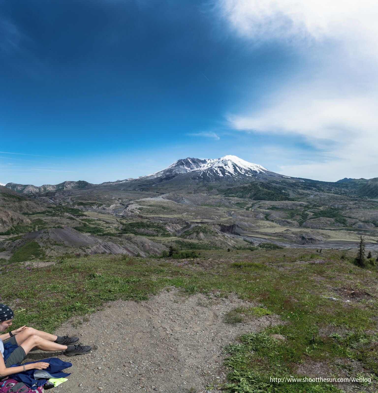 A person sitting on a gravel path with a snow-capped mountain in the background.