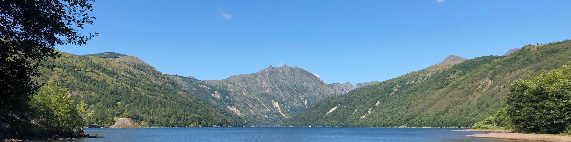 Um lago calmo, rodeado por colinas verdes e um céu azul límpido.