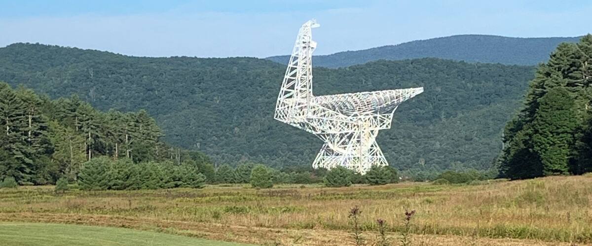 A large white sculpture resembling a bird in a grassy field with mountains in the background.