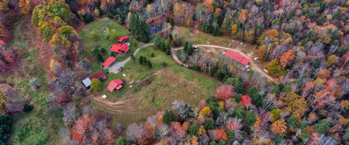 An aerial view of a rural area with red-roofed buildings surrounded by a forest with autumn foliage.