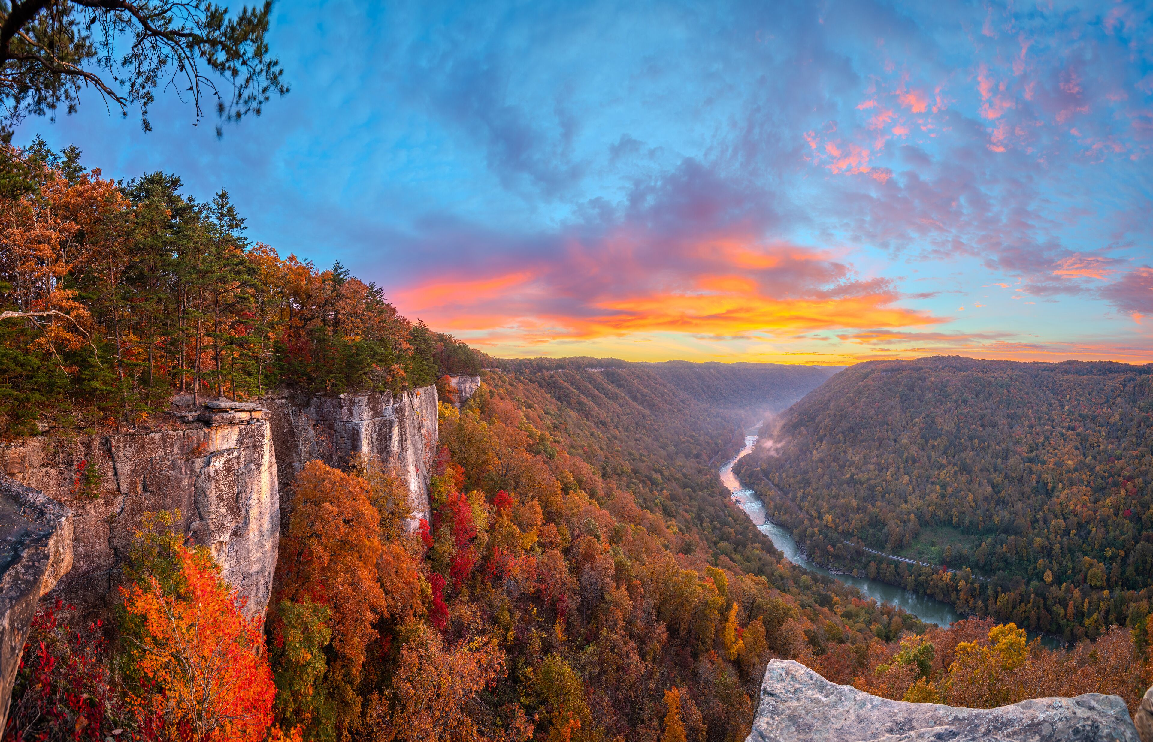 A canyon with a river, autumn foliage, and a rocky cliff.