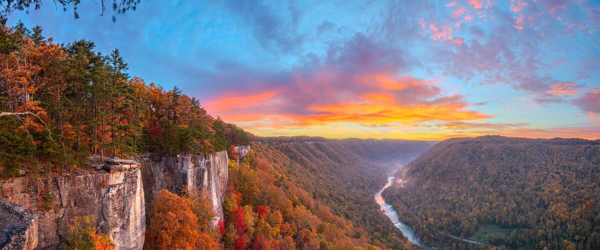 A canyon with a river, autumn foliage, and a rocky cliff.