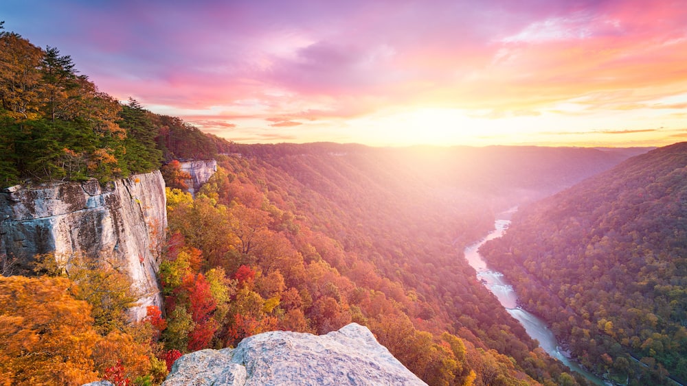 A canyon with a river, autumn foliage, and a rocky cliff.