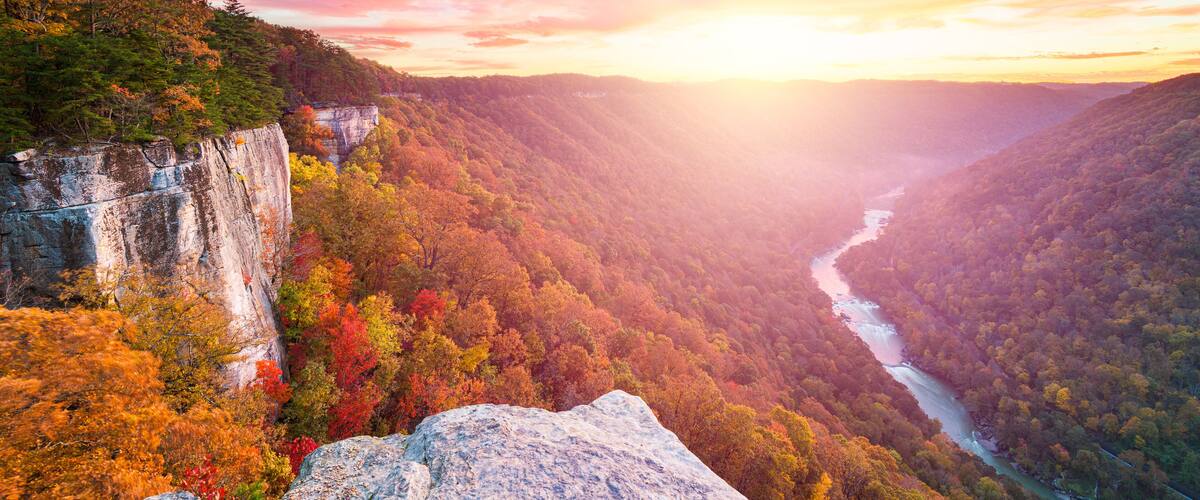 A canyon with a river, autumn foliage, and a rocky cliff.