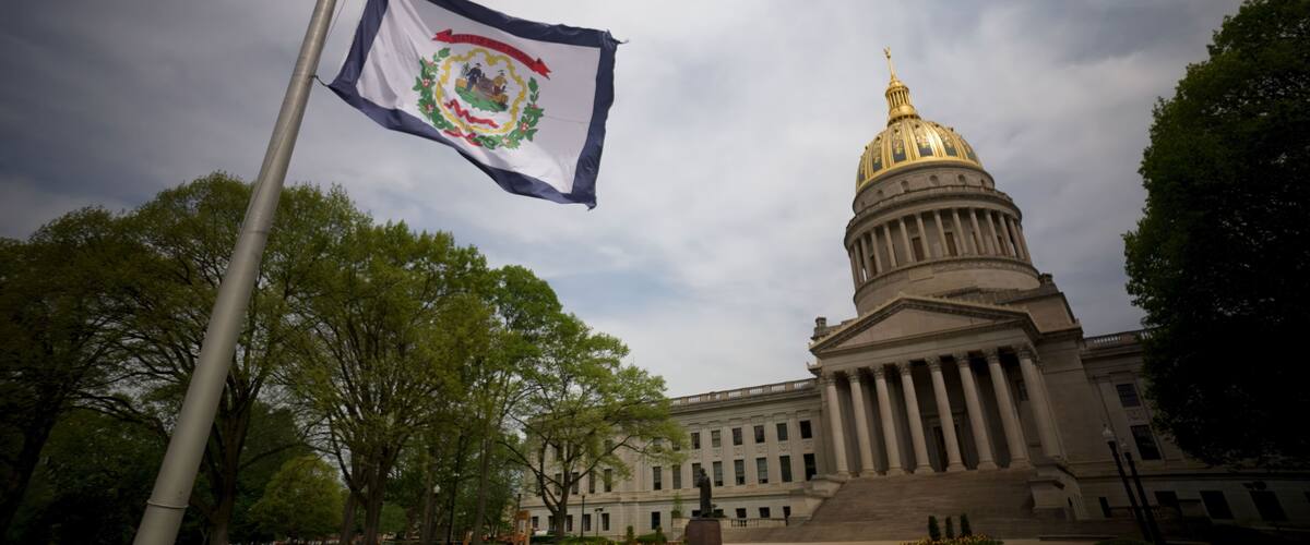 A flag on a pole, a large building with a golden dome, and trees in the foreground.
