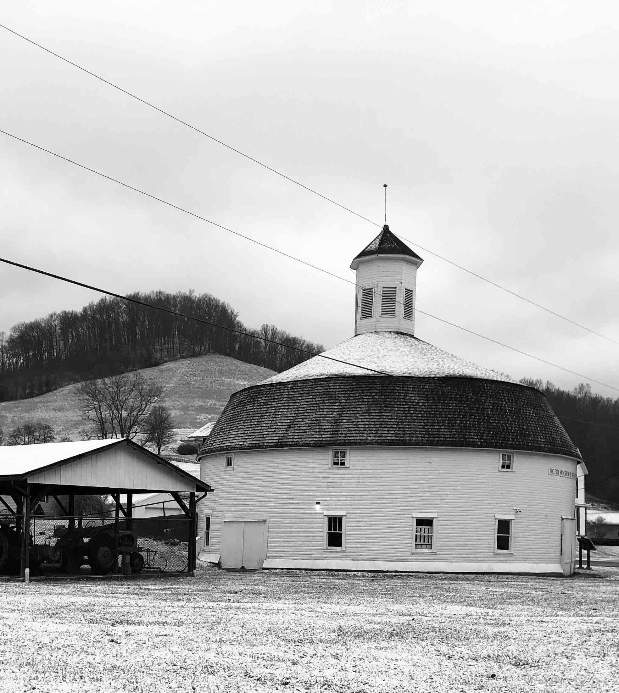 A white church with a steeple and a barn in a snowy field.