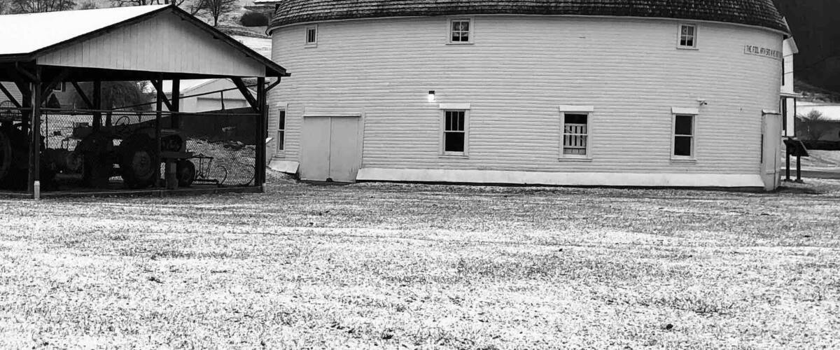 A white church with a steeple and a barn in a snowy field.