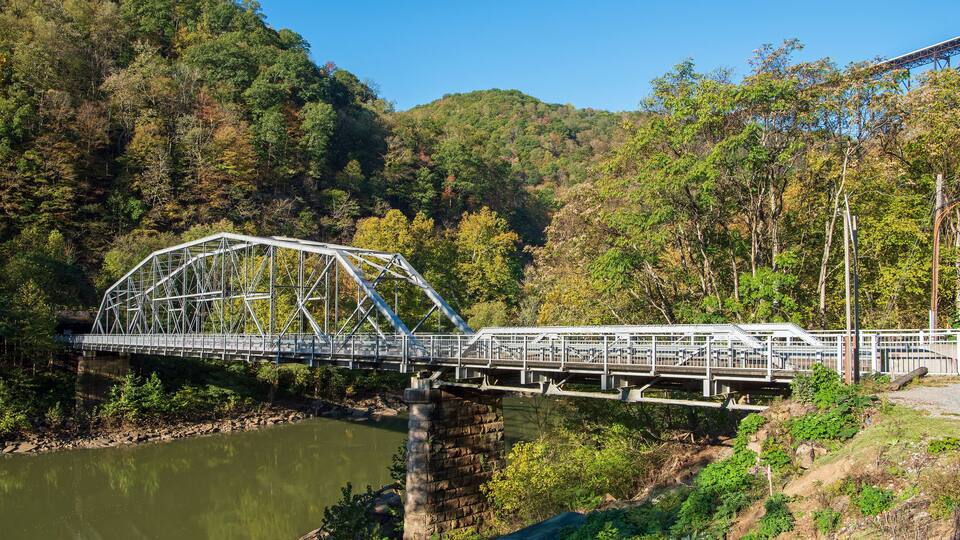 A steel truss bridge over a river with a forested hillside in the background.