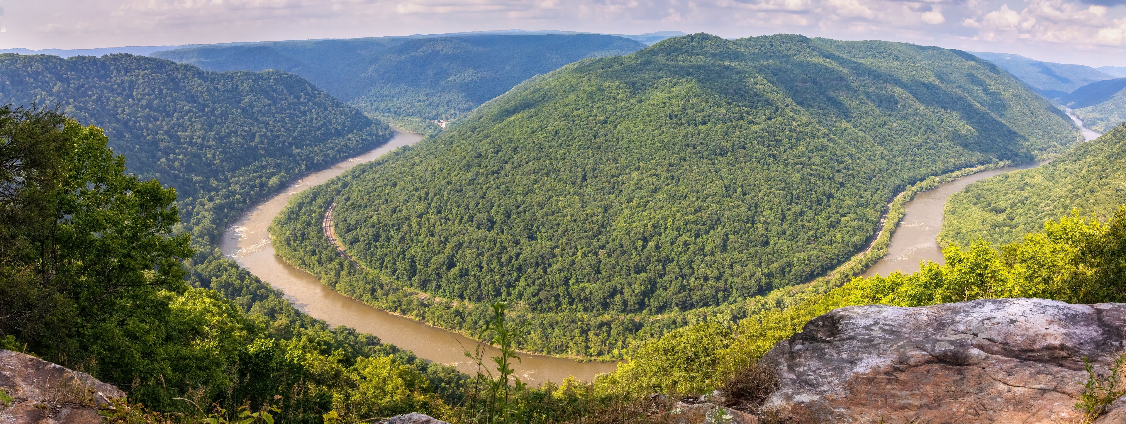 A winding river through a densely forested valley with rolling hills.