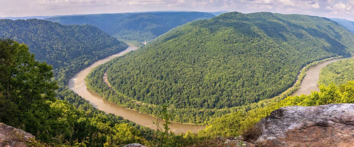 A winding river through a densely forested valley with rolling hills.