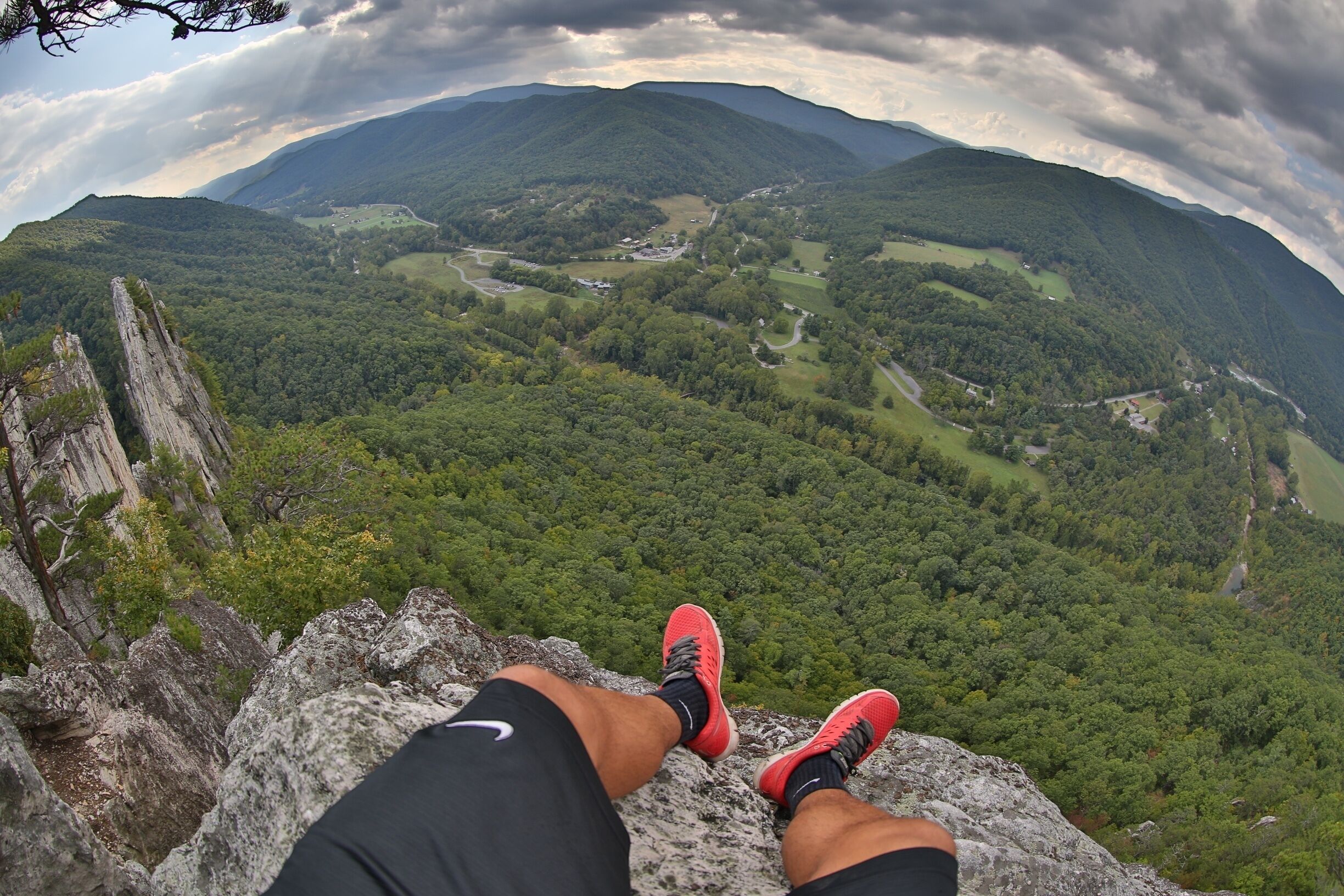 A person sitting on a rock with a view of a valley and mountains.