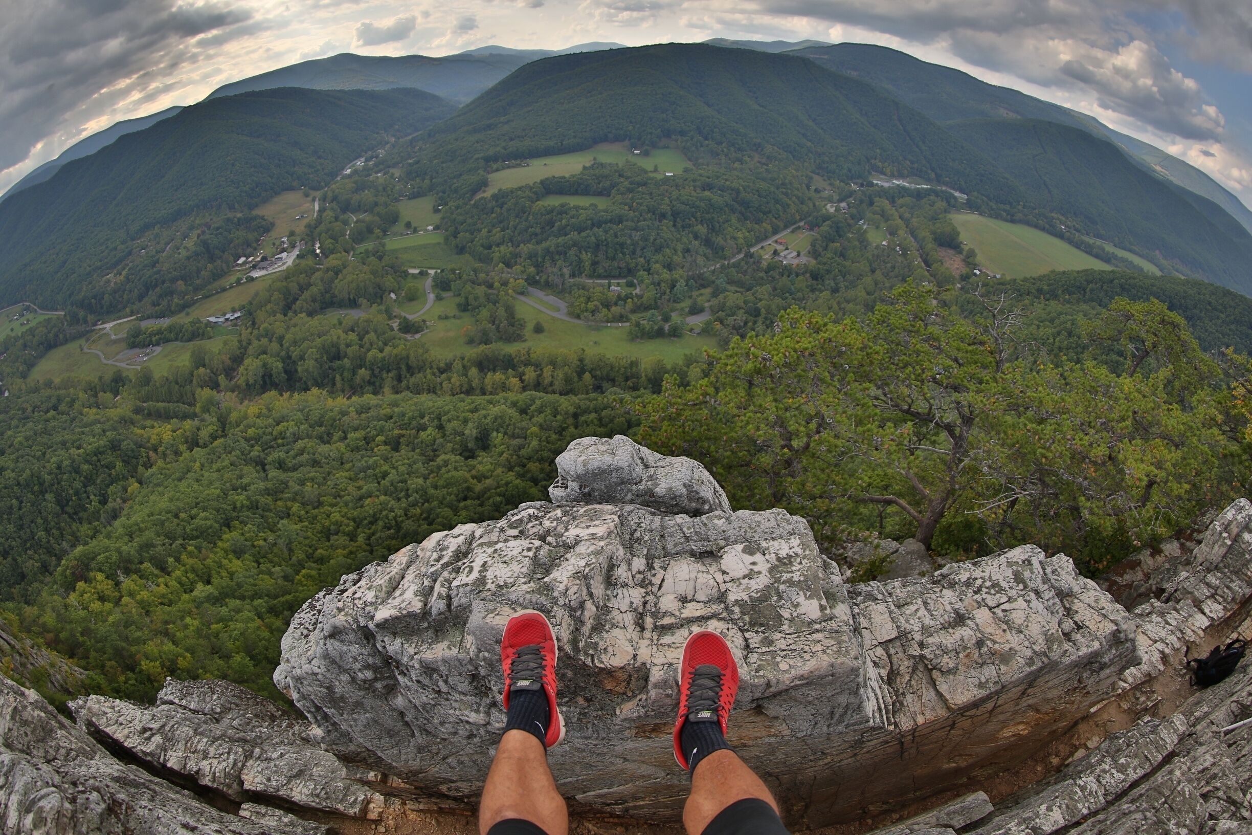A person standing on a rock with red shoes, overlooking a valley with trees and a winding road.