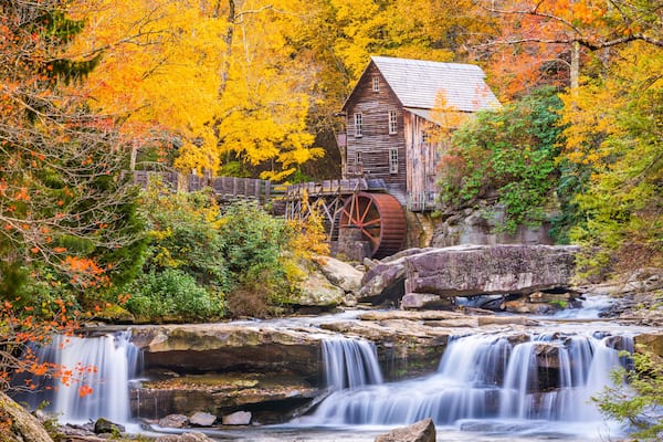 A wooden mill with a water wheel, surrounded by autumn foliage and a cascading waterfall.