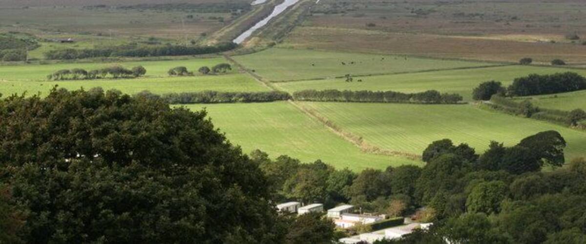 A rural landscape with fields, a road, and distant hills.