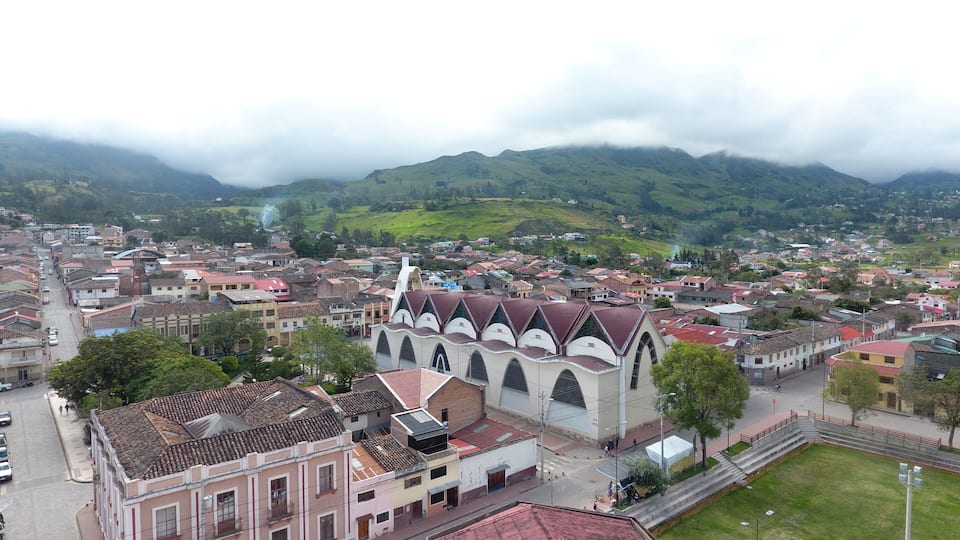 A town with a prominent church, surrounded by green hills and a cloudy sky.