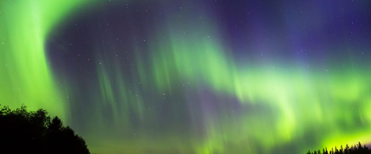 The Northern Lights over a calm lake with forested shores.