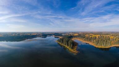 Aerial view of a clam lake surrounded by a forest of green spruce and autumn colored poplar trees.