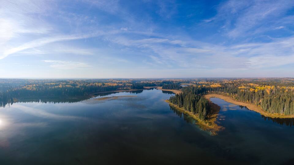 A panoramic view of a calm lake surrounded by dense forests with autumn foliage.