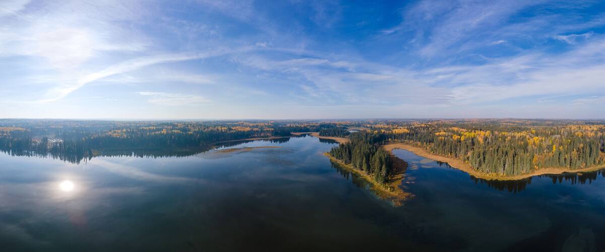 A panoramic view of a calm lake surrounded by dense forests with autumn foliage.